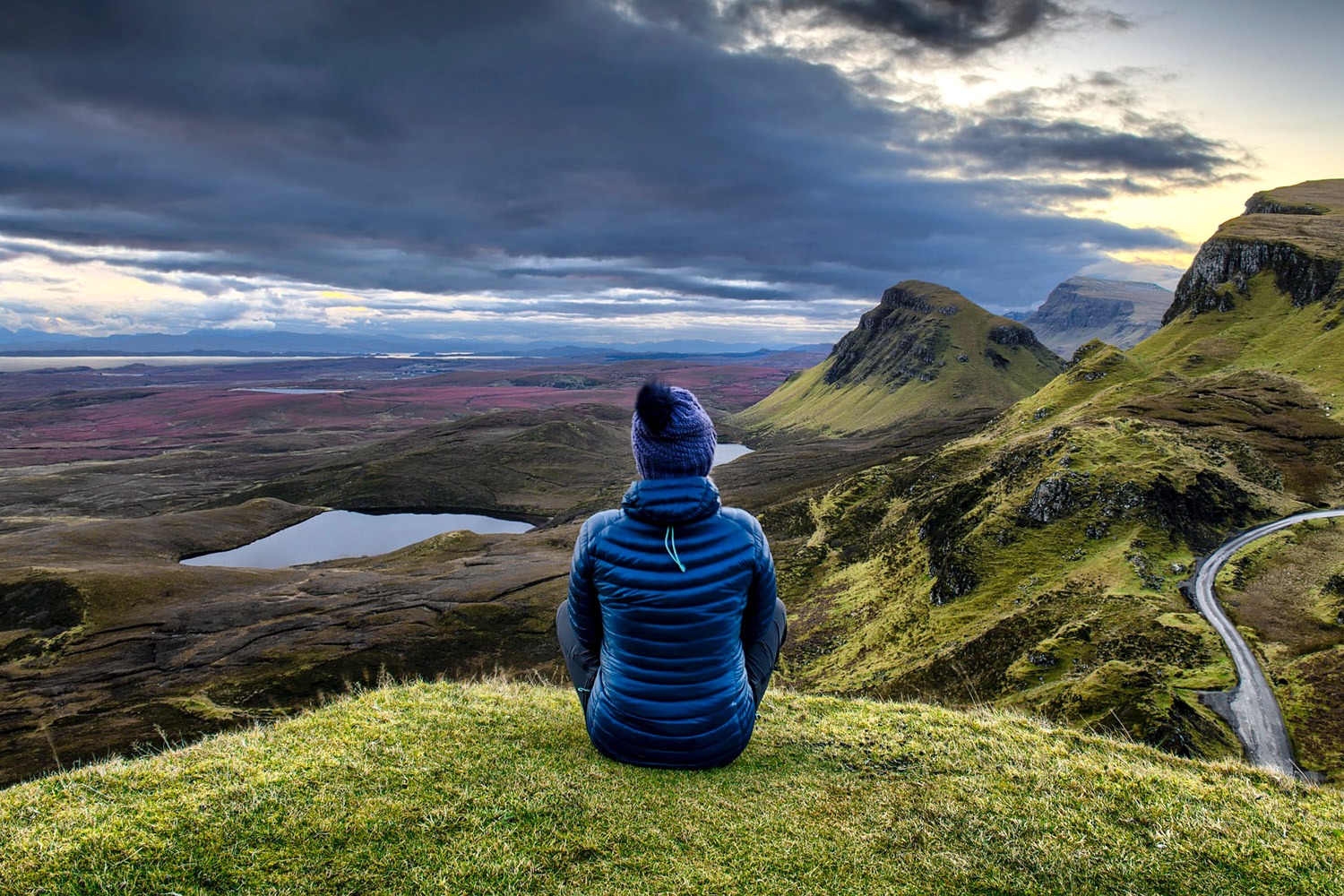 Epic vista of the Scottish Highlands mountains with a woman sitting looking at the view in the foreground. Discover Your Scottish Roots on a Custom Ancestry Tour.