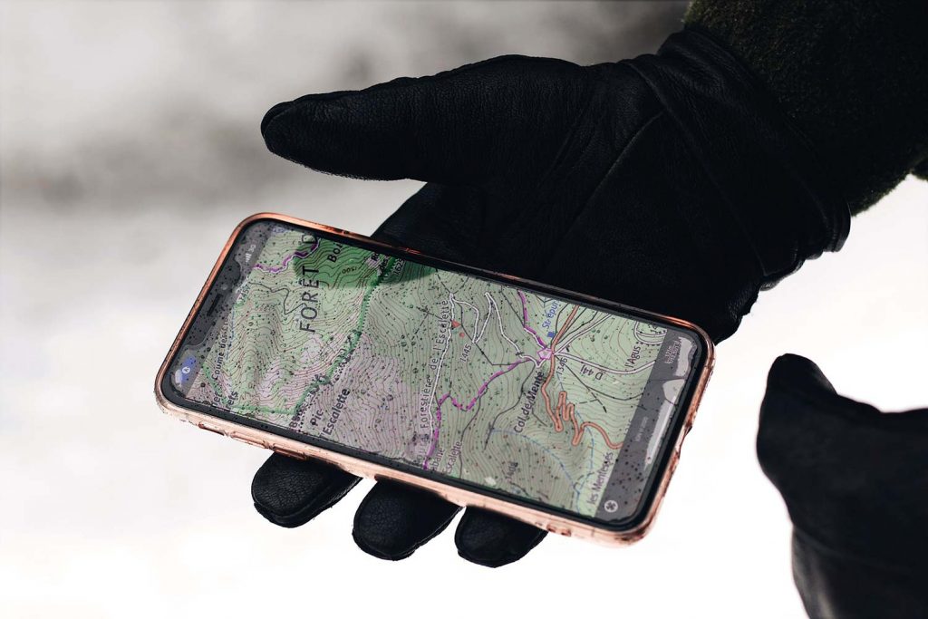 Gloved hand holding a cell phone with a GPS navigation app showing a hiking map.