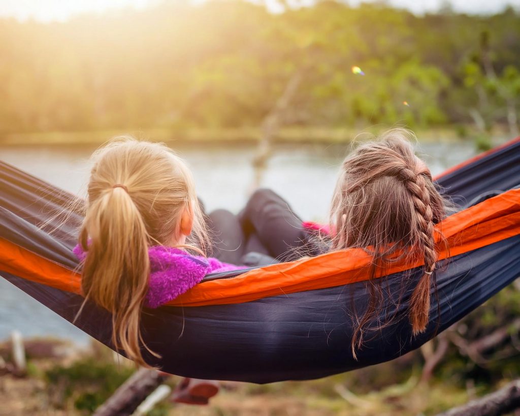 A mother and daughter swinging on a hammock looking out at a beautiful lake in the mountains.