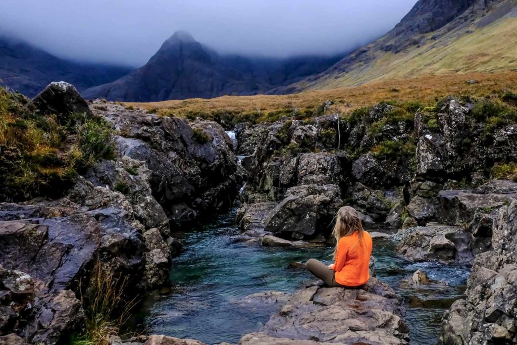 A woman sitting on a rock in the stream of a fairy pool in the Scottish Highlands.