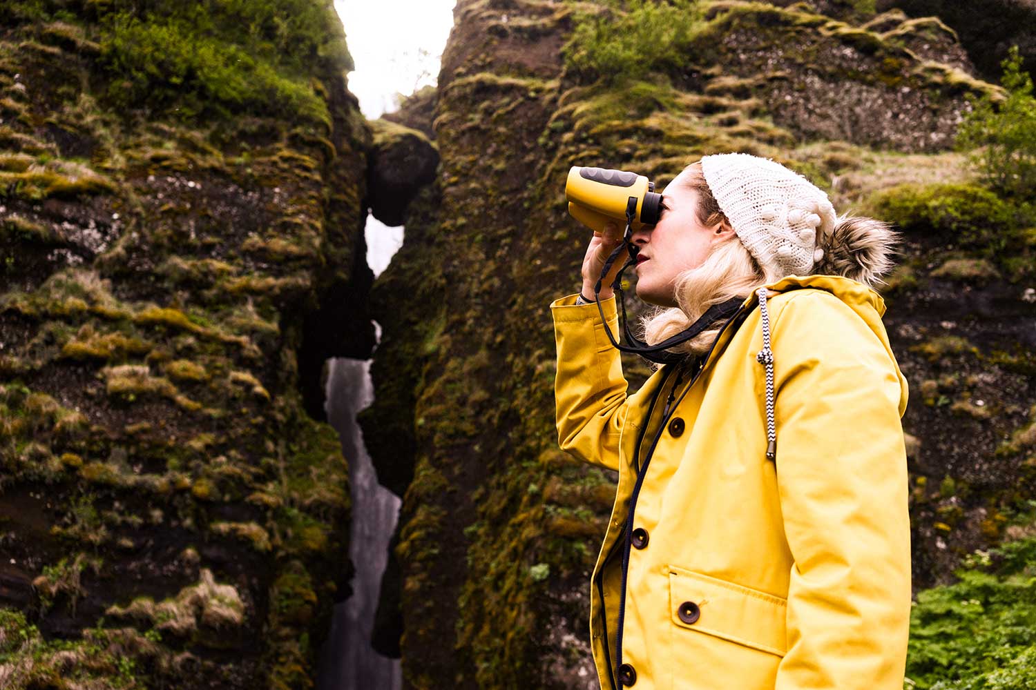 Woman in bright yellow jacket wildlife watching with binoculars.